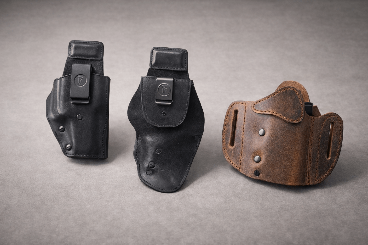 Three Urban Carry holsters arranged side by side on a neutral tabletop under soft studio lighting: a black Signature IWB holster, a black Urban Carry G3 holster, and a brown Signature OWB holster.